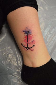 a small anchor tattoo on the right side of the leg, with watercolor paint splatters all over it