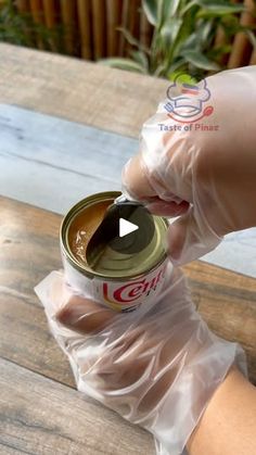 a person wearing gloves and holding a can of food in their hand on top of a wooden table