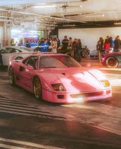 two pink sports cars parked next to each other in a parking garage with people standing around