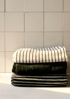 three towels stacked on top of each other in front of a white tiled bathroom wall