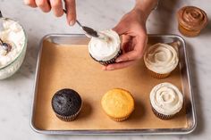 someone is decorating cupcakes with white frosting on a tray next to other cupcakes