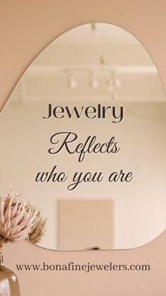 there is a mirror on the wall that says jewelry reflects who you are with a flower in front of it