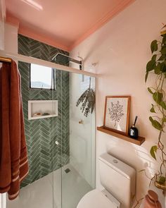 a white toilet sitting next to a shower in a bathroom under a window with green tiles on the walls