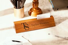 a wooden business card holder sitting on top of a desk next to a pen and paper