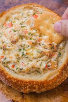 a hand holding a cracker over a piece of bread with cheese and vegetables on it