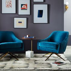 two blue chairs sitting next to each other on top of a rug in front of a gray wall