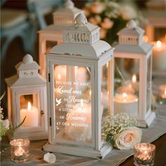 two white lanterns are sitting on a table with flowers and candles