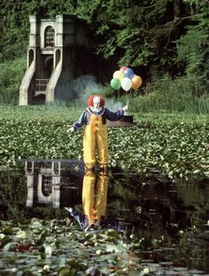 a clown is standing in the water with balloons floating above him and his reflection on the water