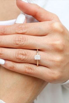 a woman's hand wearing a gold ring with a square shaped diamond on it