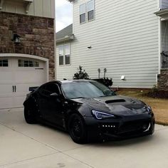 a black sports car is parked in front of a house with two garage doors on the side