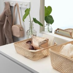 two woven baskets sitting on top of a white counter next to a mirror and purse