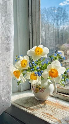 a vase filled with yellow and white flowers next to a window