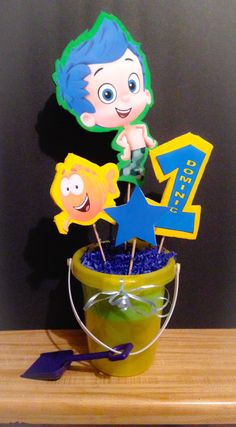 the little mermaid cake topper is in a bucket with blue and green decorations on it