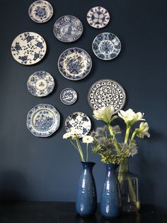 blue and white plates are arranged on the wall behind vases with flowers in them