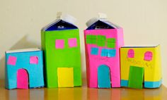 three small houses made out of paper sitting on top of a wooden table next to each other