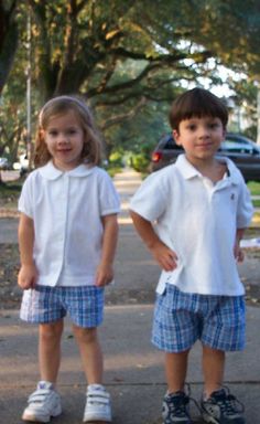 two young children standing next to each other on a sidewalk with trees in the background