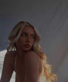 a woman with long blonde hair sitting in front of a white backdrop wearing a bra