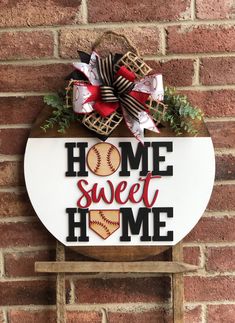 a sign that says home sweet home with baseballs and bows on it, hanging on a brick wall