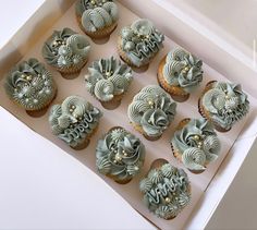 twelve cupcakes in a box decorated with frosting and gold decorations on top