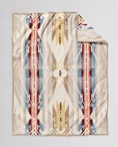 the pendleton blanket in tan, orange and blue is folded on top of a white surface