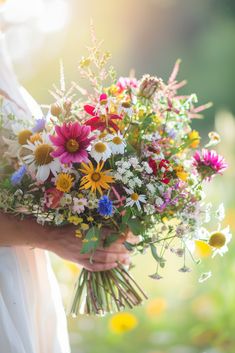 a woman holding a bouquet of wildflowers and daisies on her wedding day