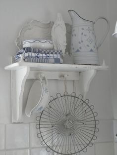 a shelf filled with dishes and cups on top of a white tiled wall next to a window