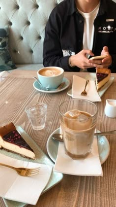 a man sitting at a table with two cups of coffee in front of him while looking at his cell phone