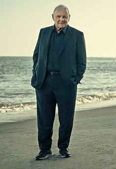 an older man in a suit standing on the beach