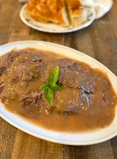 two plates with meat and gravy on them sitting on a wooden table top