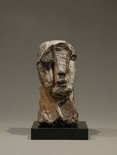 a sculpture of a man's head is shown on a black stand with a gray background