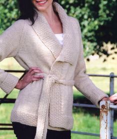 a woman standing next to a fence with her hands on her hips wearing a sweater and black pants