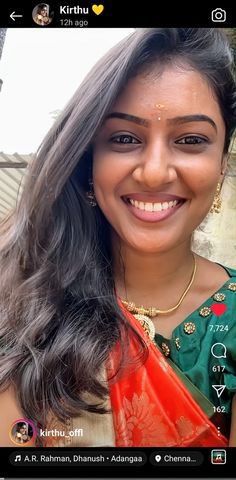 a woman with long hair smiling and wearing an orange sari on her chest, in front of a tree