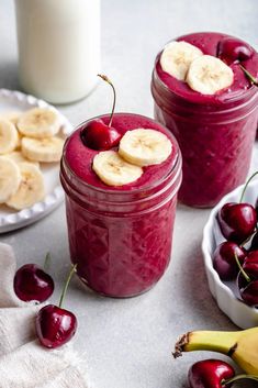 two jars filled with smoothie next to bananas and cherries