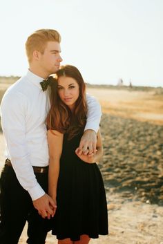 a man and woman standing next to each other on the beach with their arms around each other