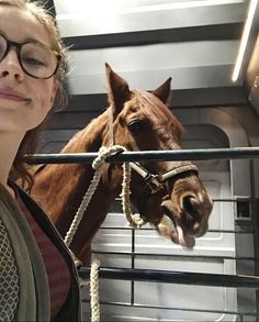 a woman standing next to a brown horse on top of a metal caged area