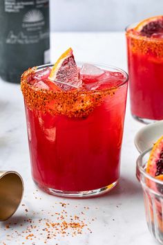 two glasses filled with red liquid and garnished with orange peels