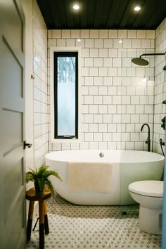 a white bath tub sitting next to a toilet under a window in a bathroom with tiled walls