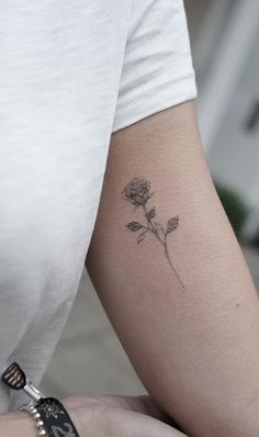 a woman's arm with a single rose tattoo on the left side of her arm