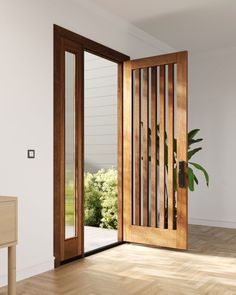 an open wooden door in a white room with wood flooring and large plant on the side