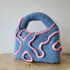 a crocheted blue purse sitting on top of a wooden table next to a white wall