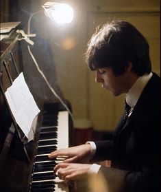 a young man sitting at a piano in front of a microphone with sheet music on it