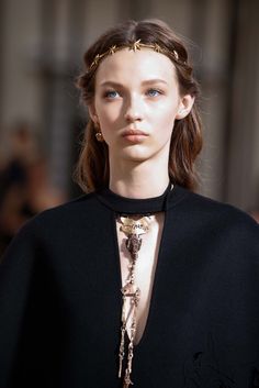 a model wearing a black cape with gold chains on her head and shoulders, looking off to the side