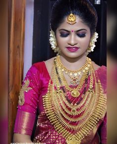 a woman in a red and gold saree with jewelry on her neck, looking down at the camera