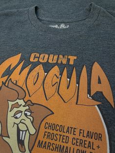 I Want To Eat Your Cereal! I want to eat your cereal! Count Chocula isn’t your average vampire, he is a chocolate loving, cereal eating vampire! Introduced in 1971, this seasonal cereal was seen in the fall with other Monster cereals like the strawberry flavored Franken Berry. The Count shown here is very retro, and printed on a Charcoal Heather tee with a light distress over the print. You may become nostalgic while wearing this tee, so next fall stock up on the chocolaty cereal because this sh Cereal Logo, Cereal Logos, Count Chocula Cereal, Monster Cereal, Franken Berry, Count Chocula, General Mills, Retro Graphic Tees, I Want To Eat