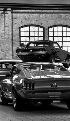 two mustangs are parked next to each other in front of large windows and brick buildings