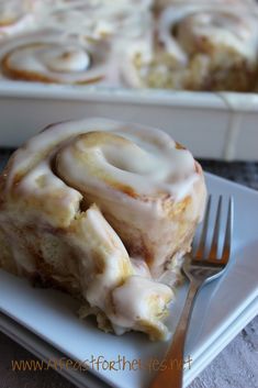 a close up of a plate of food with a fork on it and a pan of cinnamon rolls in the background