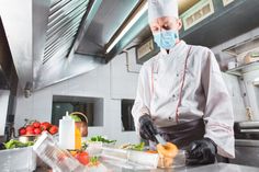 a man wearing a face mask and gloves preparing food in a kitchen with vegetables on the counter