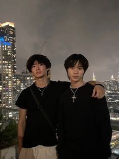 two young men standing next to each other in front of a cityscape at night