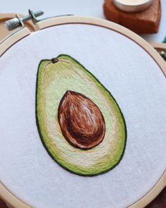 an avocado embroidered onto a white fabric with a wooden hoop next to it