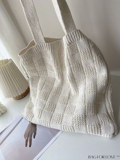 a white knitted bag sitting on top of a table next to a vase and lamp